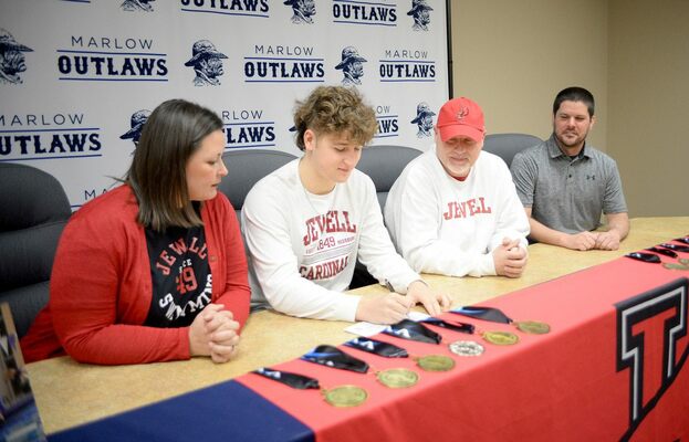 Marlow High School senior Gage DaVoult signs his letter of intent to swim at William Jewell College in Missouri, as his parents Chelsea and Gary watch, along with former Coach Andrew Bowers, Monday, Feb. 20, 2023. Photo by Toni Hopper/The Marlow Review